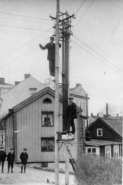 Överst på stolpen Stadsmontör Hilding Jansson. Nederst Nils Jansson Montör , dragspelare. Pojkarna från vänster 1 Maurits Sköldborg Chaufför, 2 Holger Jansson  Elektriker,  3 Ragnar Liljegren Smed. Huset närmast är Maja Petterssons. bakom detta är Vickbergs och Stadshotellet.   
Rönnbärsgatan / Norrtullsgatan