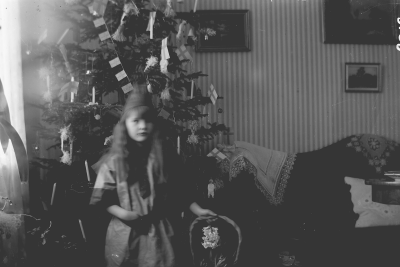 Flicka stående vid julgran. Elsa Blomberg född Hallberg som jultomte på Storgatan 5 Vimmerby år 1919.
