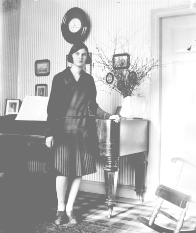 Kvinna står vid ett piano. Elsa Blomberg född Hallberg, Storgatan 5, år 1928.