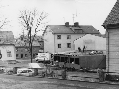 Gamla Samskolan och dess tillbyggnader rives när Kvalitetsmöbler bygges. Bakom möbelbil, Lisbeth Jonssons kiosk. Skogsbergs manufakturaffär mittöver gatan, på övervåningen bodde skomakare A.P.Hallberg. Längst till vänster , mjölkbutik på 1940-talet, senare Gatukök, så Brödstugan och nu Pizzeria Palma.