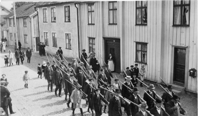 Skyttekåren paraderar på Storgatan.15 Wallin, 19. Ludvig Pålsson, 20. Skomak. Västerberg, 25 Fru Ebba Dahl, 28. Oskar Johanson, 29. Axel Ståhl, fabrikör, 33 Bertil Westman, 38 Fritz Högman ( arbetare hos Ståhls möbler ), 40. Albert Borgstrand, 42. Ture Hammargren,  44. Nilsson, smed, 49 Garvare, Österman.     