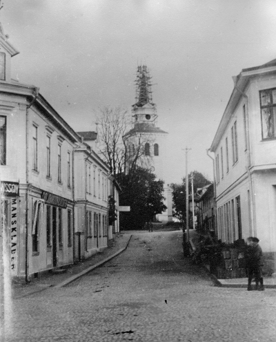 Åsknedslag 5 nov 1911 reparation sedan. Carl Johanssons Manufaktur tilll vänster. Nästa hus t.v. på övervåningen bodde Dr Hellström. Nedre våningsplan inrymde ett kafé kallat "Tre flickorna".
Huset längst upp t.v. inrymde telegrafstation på andra vån. På nedre plan hade Rickard Olsson Herrekiperingsaffär. Den fanns där 1929. Numera museét Näktergalen. I hörnet t.h. på Sevedegatan - Torget fanns en modeaffär och t.h. därom Rudells skoaffär.		      