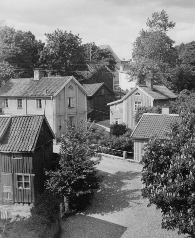 Kampbacken sedd från Storgatan. Kastanjen planterades på 1900- talet i det hål som tidigare var vattenreserv innan staden fick vattenledning.
I tvåvåningshuset till vänster bodde fru Elsa Wahlsten, glansstrykerska, bland annat stärkte och strök hon frackskjortor, dukar  m.m. Hon hade även taxirörelse med 2 bilar, Börje Söderberg var chaufför för en av dom.
I huset inne på gården bodde familjen Hultin. Det röda mörka huset närmast till vänster inrymde Harry Franssons skomakeri.
Uppgiftslämnare: Vera Liljeblad, Granen/GS 021113

Dok.090205/SJ