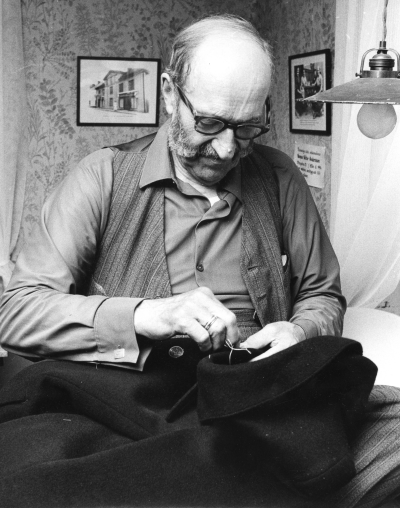 Ur Vimmerby Tidning 22 juli 1972.  Gästgivarhagen utrustad med skräddareverkstad. Skräddarmästare Jakobsson, död 1981, visar här hur han arbetade i den gamla skräddareställningen, sittande på bordet. Gästgivarhagen i Vimmerby har nu fått sin åttonde hantverkarverkstad. Den åttonde blev ett fullt utrustat skrädderi och det är skräddaremästare Eric Jakobsson som har överlämnat sin verkstad. Skräddaremästare Eric Jakobsson, 81 år, upphörde med sitt skrädderi i Vimmerby den 1juli i år. I och med det upphörde Vimmerbys siste beställningsskräddare med sin verksamhet. Skräddaremästare Jacobsson föddes i Nykyrka socken i Mullsjö i Skaraborgs län. Han började i skräddaryrket redan i 15-16 årsåldern hos sin far. Till Vimmerby kom han 1925 och började då arbeta hos Gustaf Dewinger som tillskärare. 1934 startade han egen verksamhet på Storgatan 50, där sedan skrädderiet varit beläget. Nu har han alltså överlämnat skrädderiet med inventarier till Sevedebygdens fornminnes- och hembygdsförening som monterat upp verkstaden i Östra Tullportsstugan i hembygdsparken i Gästgivarhagen.   