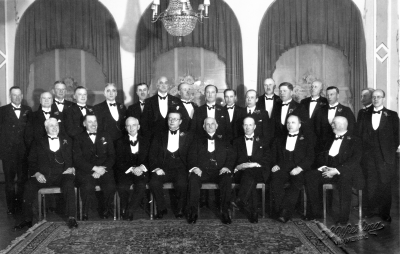 Pro Patria till Almér, Rudell   Taget på stadshotellet sittande från vänster 1. Nils Ståhl, fabrikör 2. Simon Andersson, köpman 3. Erik Rudell, köpman 4. Ragnar Odevall, borgmästare 5. Axel Almér, plåtslagare 6. Frans E. Norén, borgmästare 7. Mauritz Malmström, rektor 8. Erik Ingeström, bankdirektör 9. Albin Carlsson, 10. Albert Borgstrand, skomakare 11. Tor Melander, murare 12. Johan Castenfors, läkare 13. Emil Severin, häradshövding 14. Axel Lindblad, smed 15. Carl Erland Benzer, lantmätare 16. Edvin Gabrielsson, skogvaktare 17. Theodor Hellström, läkare 18. Arvid Karlsson, kamrer 19. Carl Carlsson, kassör 20. Axel Lindström, köpman 21. Sigurd Gustavsson, byggmästare 22. Ernst Lundahl, stadsfiskal 23. Erik Hallberg, fabrikör 24. Emil Larsson, brevbärare 25. Vilhelm Winell, stadsingenjör.  