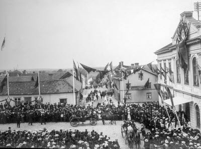 Kungabesöket då järnvägen invigdes. Oscar II och kronprins Gustaf anländer till stadshotellet.   
Låga huset till höger inrymde Rudells skoaffär (till höger) och ölstuga till vänster. På nedre våningen i huset till höger fanns bibliotek och värmestuga. (Uppg Malmberg)