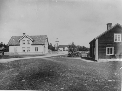 Rumskulla kyrka sett från söder 1907-08 Från vänster,  Petterssons affär, till höger gamla fattigstugan sedan och bostad för barnmorska, samt telefonstation och bostad.