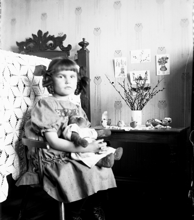 En flicka med en nalle i knäet. Elsa Blomberg född Hallberg Påskpyntat. Storgatan 5.