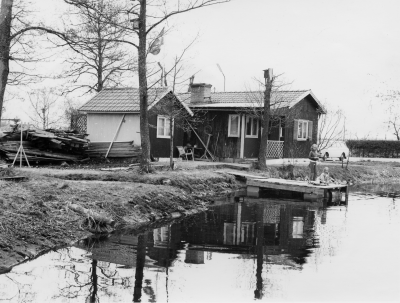 Kurt Helanders hus vid branddammen Ö. Tullportsgatan 1960-talet. Kurt Helander fru Lilly född 1906 har berättat att Knut byggde av rivningsmaterial. Folk "skrattade" åt hans bygge. Kalle i Ekehill byggde huset. Knut och Lilly bodde där i 40 år. Knut jobbade åt kommunen bl.a. som dammvakt. Skötte flödet genom dammluckorna. Flickorna på bryggan är barnbarn till Lilly, Ann Christin och Ann Charlotte.