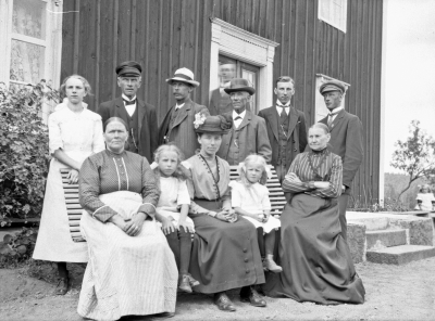 Sittande från vänster: Ida Sofia Persdotter född 1860 17/4 i Hjorted död 1946 18/10 i Västra Grinderum Frödinge, Stina född 1905 12/12 i Västervik, Hedvig Johansson född Nilsson 1875 död 1938 20/2 i Hermanstorp Västervik, Margit född 1909 22/6 i Västervik, Kristina Maria Svensdotter född 1846 i Kvarnäs i Tuna död 1917 i Hermanstorp Västervik. Stående från vänster: Karin född 1899 11/8 in Törnsfall, Johan August Johansson född 1858 och död 1925 i Västra Grinderum Frödinge, Karl Johan Oskar Johansson född 1872 i Frödinge, Frans Oskar Johansson född 1850 i Västra Grinderum Frödinge död 1922 i Hermanstorp i Västervik, Gustav Wirenfeldt född 1897 i Västervik, Per Ludvig Johansson född 1887 och död 1926 i Västra Grinderum Frödinge. Detta är alltså ett släktfoto med två bröder: Johan August Johansson och Frans Oskar Johansson samt deras familjer. Ida Sofia gift med Johan August och Kristina Maria med Frans Oskar. Per Ludvig är son till Johan August och Ida. Karl Johan Oskar Johansson är son till Frans Oskar och gift med Hedvig och med på bilden är deras fyra barn. Skuggfiguren längst bak är oidentifierad. Fotot är taget i Västra Grinderum hos Johan August Johansson.  M.K.