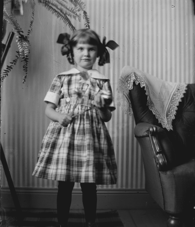 Flicka stående vid fåtölj. Elsa Blomberg. Storgatan 5.