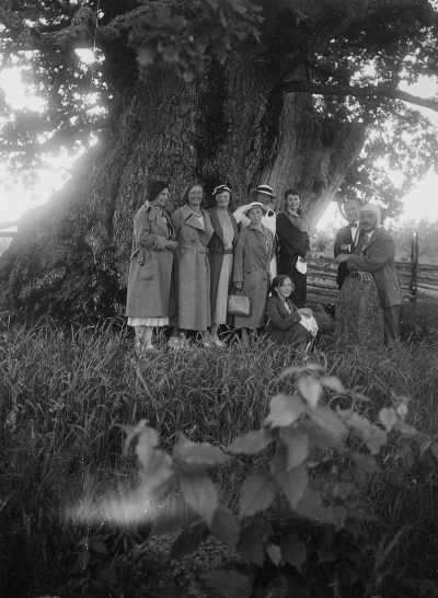 Tusenåriga eken i Norra Kvill. Lis-Karin o Aina Ängqvist, Oskarshamn,  Tekla Carlsson, Knabbarp,  Sigrid Wahlberg,  Ester Karlberg, Malmö  Fru Karlberg och Robert Karlberg och  Erik Wahlberg.  På marken Karlbergs barnjungfru.          