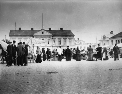 Rudells hus var nybyggt det året! I klungan till vänster två herrar i plommonstop den till vänster  Axel Karlsson ( fjärdingsman ), Ödestorp, till höger Emrik Karlsson ( bror till Axel), vägmästare. Damen i mitten med vit jacka, Fröken Anna Thisell, damen till höger Hilda  Barkman, gift med Rådman Gustav  Barkman, mor till Rådman John Barkman.