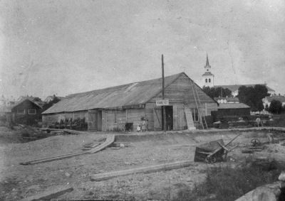 Tillfälliga Stationshuset. Artikel: Ett Unikt Stationshus.  Det är ju inte så ofta, som det goda Vimmerby gör något väsen af sig. Det är i allmänhet ett lungt och stilla samhälle. Men i dagarna har Vimmerby låtioti starkt tala om sig. Saken är nämnligen den -- att stadens stationshus i dagarne flyttats (rullats) till sin nya plats, en bit närmare staden. Medan detta naturligtsvis rätt omständiga flyttningsbestyr pågår, äro expedition, telegraf m.m. inrymda uti ett större skjul, hvars trätak höljts med enpresenning, så att det
ej skall rägna in i "expeditionen" och "väntsalen". Utanför, på en telegrafstolpe, är upphängd en trätafla med stationens namn. Där nere i träsket, bland grus, sten och träribbor finnes "plattformen", hvilken sistnämnda utgöres af timmerstockar -- allt så primitivt och sommarsvalt som möjligt