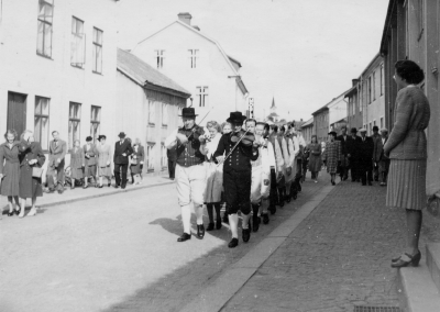 Spelmännen är fr.v. Gustaf Lindqvist Kisa, Paul Lind Vimmerby mitt i bilden tittar Gunnar Nilsson fram. Stora vita huset till vänster på storgatan är före detta färg och redskap. Uppgiftslämnare: Karin Pettersson 030212.