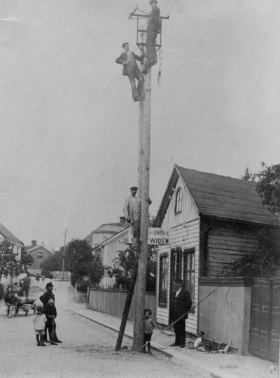 " Norrtullsgatan omkring 1920-talet, på marken längst till höger stadsmontör Hilding Jansson, andra man på stolpen är Arne Sköldborg och nederst Karl Johan Beijer. Widéens ateljé brann 1929 överst i stolpen ?  Erik Karlsson "Uggla"? Mannen på gatan till vänster Karl Fransson Stenhuggare gossen vid stolpen Erik Beijer son till Karl Johan Beijer.