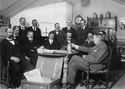 Vimmerby Fabriks o. Hantverksförening i dess lokal vid Västra Tullen. Från vänster  1 Oskar Wenström Kopparslagare,  2 Anton Vesterberg Skomakare,  3 Ture Hammargren Urmakare,  4 Oskar Johansson Sadelmakare,  5 Konrad Jönsson Charkuterist,  6 Axel Ståhl Möbelfabrikör,  7 Erik Ringholm Kakelugnsmakare  8 Okänd  9 C.O. Wallin Skomakare, kyrkvärd, 10 Arvid Srömdahl  Målarmästare,  11 Ernst Österman Garvare (Ernst  Fabian),  12 Ludvig Påhlsson Guldsmed, 13 ?  Bandet och pistolen ( till höger i bild ) finns i Gästgivarhagen.