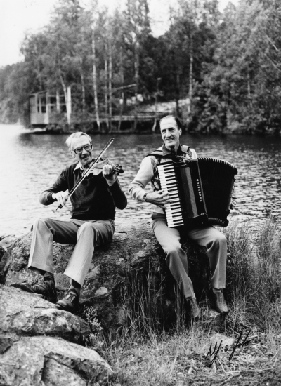 Allan Jonssons egen dokumentation:  "Allan Jonsson och musiklärare Freddy Lönngren. Storbro dansbana i bakgrunden, kortet taget i samband med inspelningen av LP-skivan "Efter Balen" vid Tomtelius studio i Storebro. Freddy och Allan spelade ihop i 20 år, på bröllop, 50-års kalas, enskilda fester och midsommardanser. Jag har varje år utan något uppehåll i 43 år, spelat i Gästgivarhagen och Källängsparken."