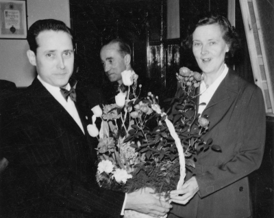 Yrkesskolan styrelseordförande Olof Lindblad överlämnar blomman till fru Brantemo,   Ossian Åberg Vimmerby i bakgrunden.    